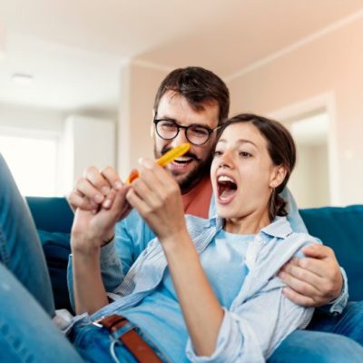 Paar mit Babyfütterung, lachend auf Sofa, Schwangerschaft Vorbereitung