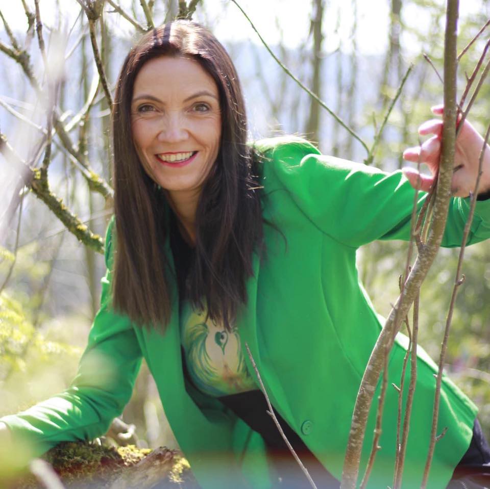 Carmen Duffner lächelnd in grüner Jacke zwischen Weidenzweigen im Wald