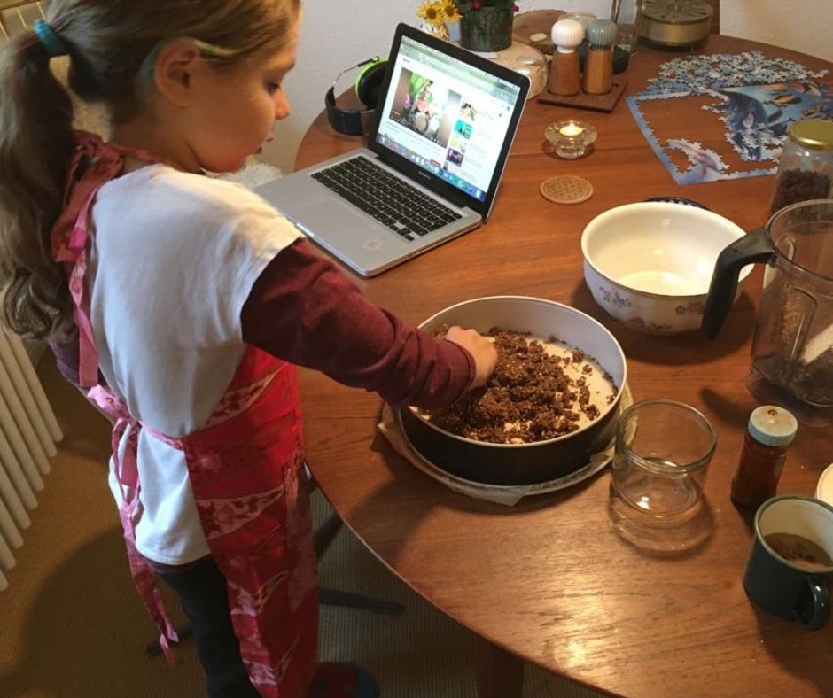 Mädchen von hinten an Holztisch mit Laptop und Schüssel voller brauner Masse, Kochsituation