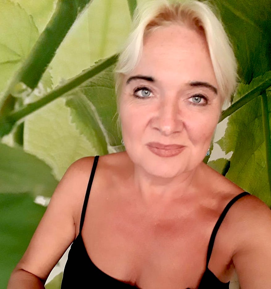 Porträt einer älteren Frau mit platinblondem Haar vor grünem Efeu-Hintergrund
