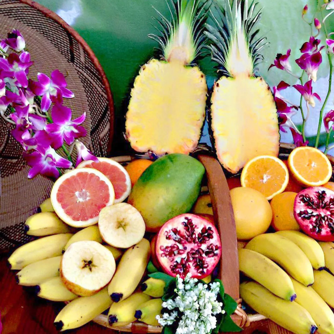 Kunstvoll arrangierte Obst- und Blüten-Stilllife mit Ananas, Bananen, Mango, Granatapfel, Zitrusfrüchten, Orchideen und Kokos