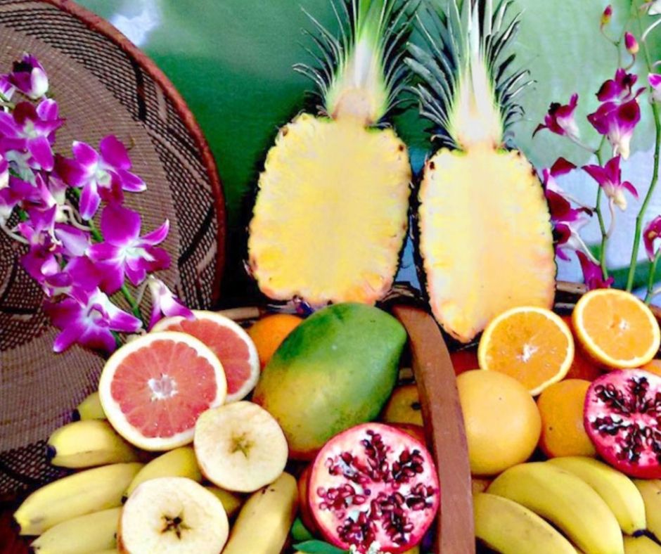 Kunstvoll arrangierte Obst- und Blüten-Stilllife mit Ananas, Bananen, Mango, Granatapfel, Zitrusfrüchten und Orchideen