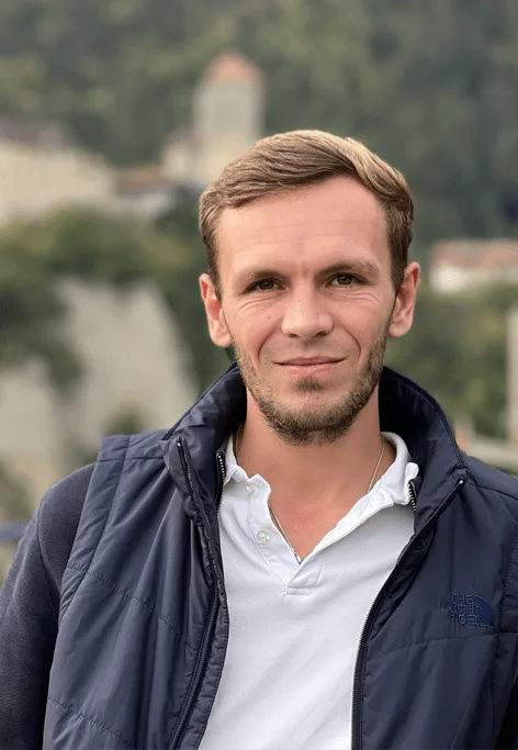 Porträt eines Mannes mit kurzen braunen Haaren und Bart vor unscharfem Berglandschaftshintergrund