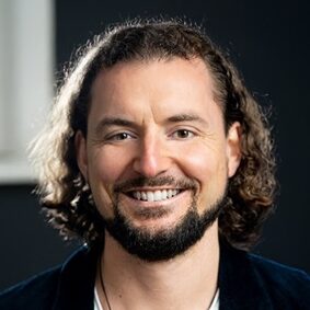 Porträt Sören Schumann mit lockigen dunklen Haaren und dunklem Anzug