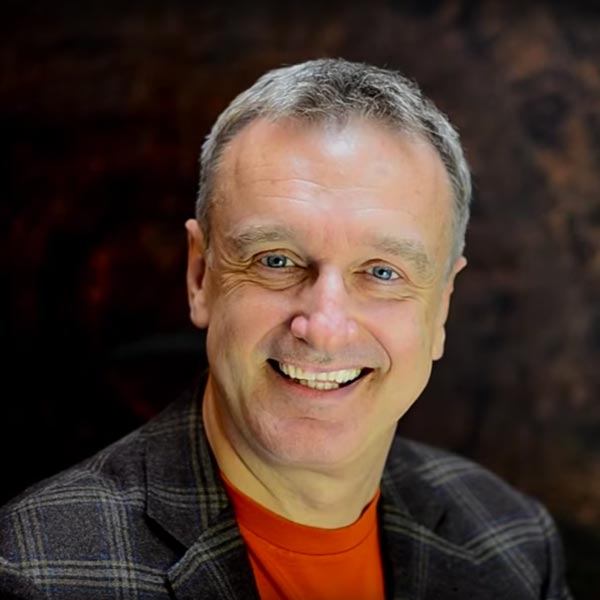 Porträt von Chris Mulzer, mittelalter Mann mit grauem Haar, lächelnd, schwarze Jacke über rotem Shirt