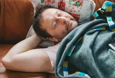 Schlafender Mann auf braunem Sofa mit Decke