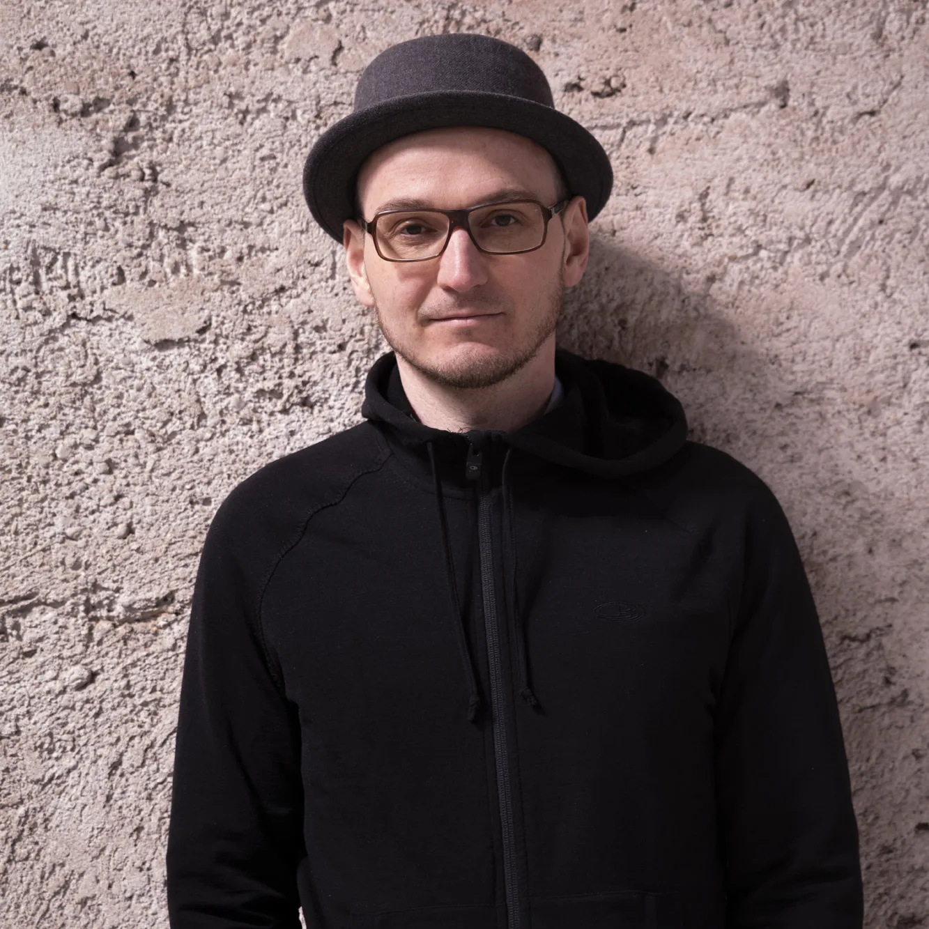 Dipl.-Ing. Architekt Bernhard Kurz in schwarzer Jacke und Hut vor Betonwand