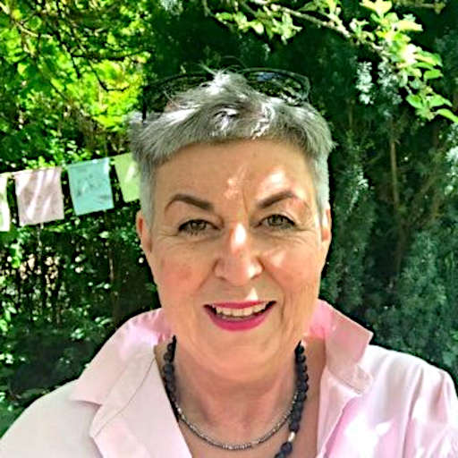 Christine Fuchs, ältere Frau mit grauen Haaren und rosa Shirt vor Efeu-Hintergrund