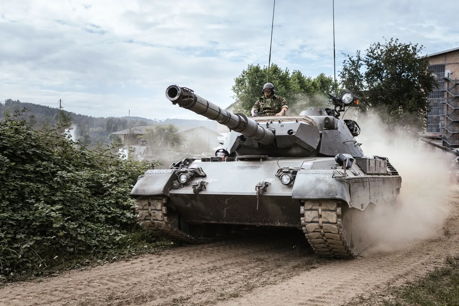 Militärischer Panzer fährt durch staubiges Gelände mit Soldaten und Gebäuden