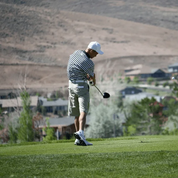 Golfer beim Abschlag in Berglandschaft mit gestreiftem Shirt und Kappe