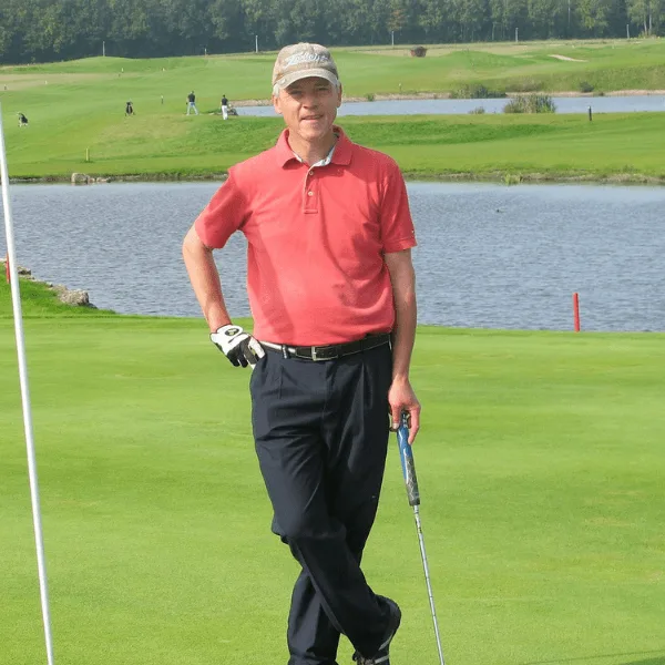 Golfer in rotem Polo-Shirt und Kappe auf Golfplatz mit Wasser im Hintergrund