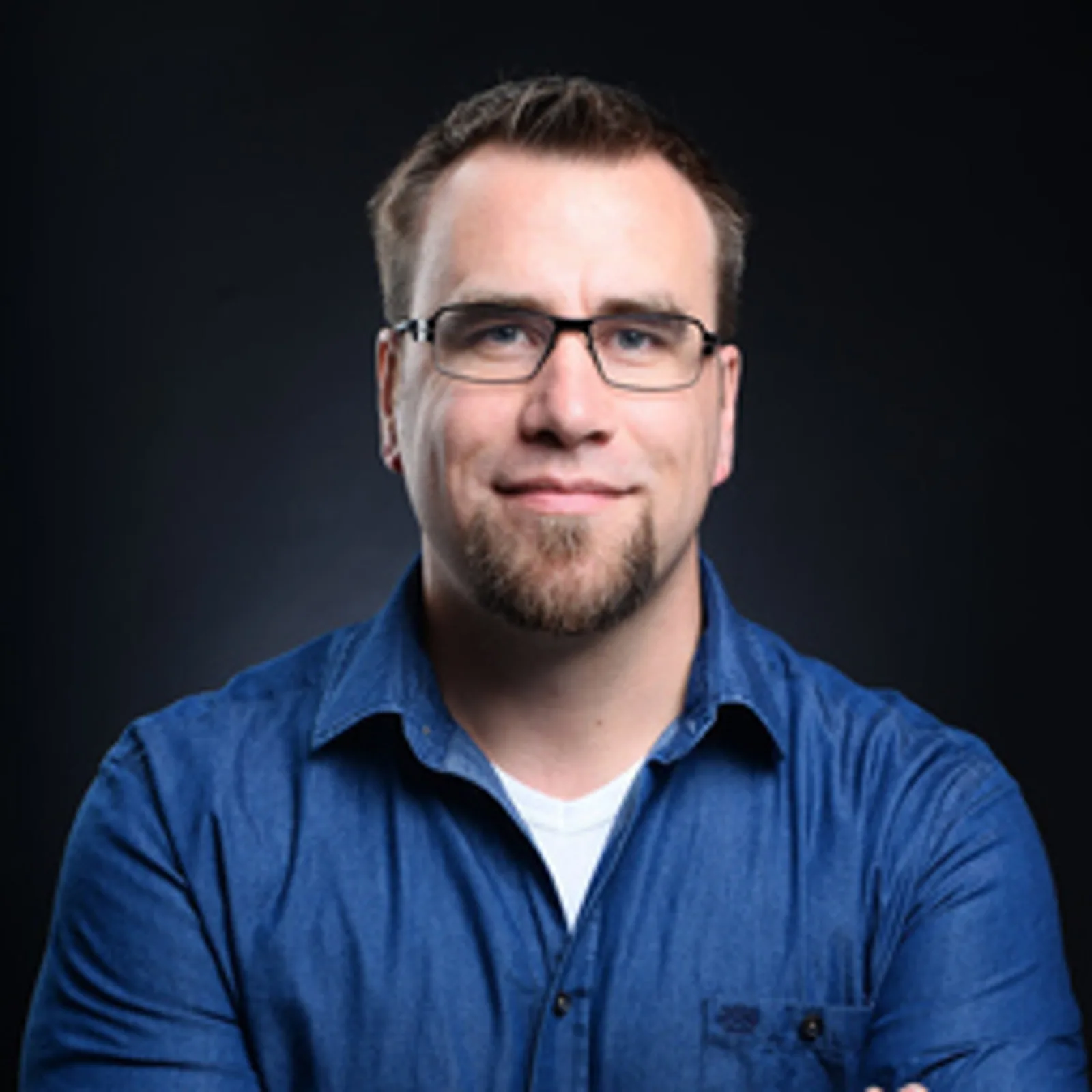 Grundlagen und Praxis der IT-Sicherheit nach DIN 27076 7 Porträt eines jungen Mannes mit Brille und blauem Hemd vor dunklem Hintergrund