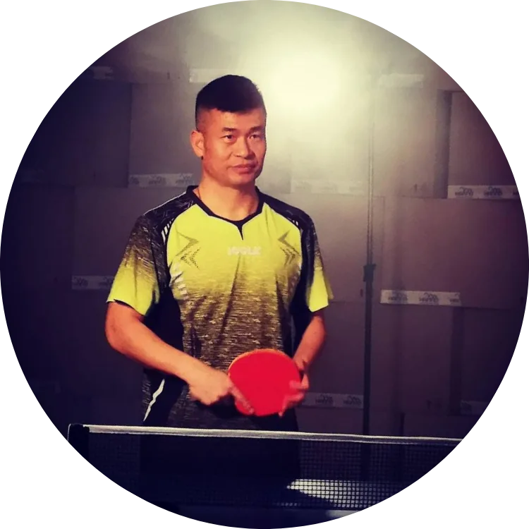 Junger Mann in gelbem Tischtennisshirt mit rotem Schläger an Tischtennisplatte