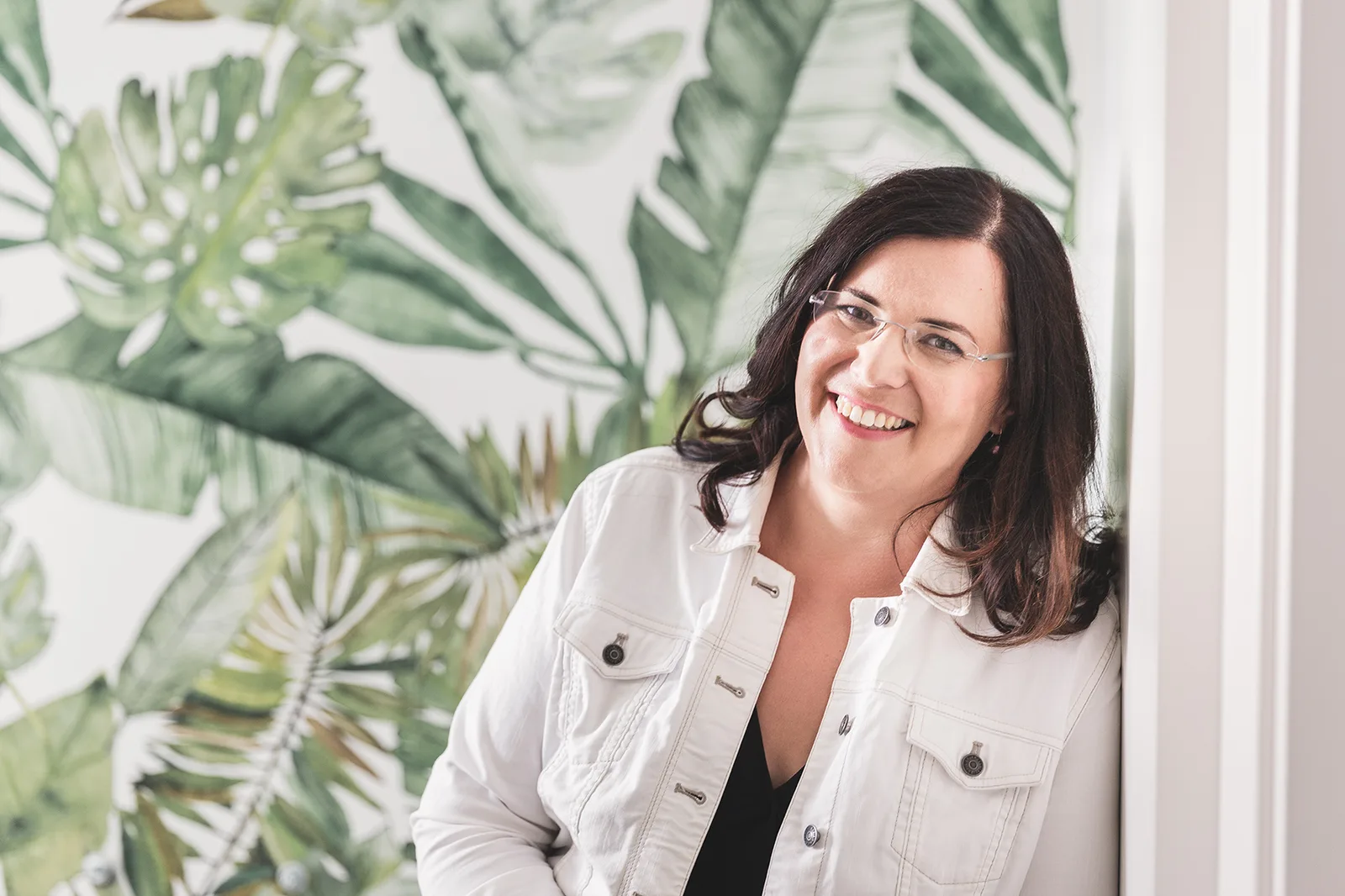 Maria Husch Porträt mit Brille und weißer Jacke vor Pflanzenwand