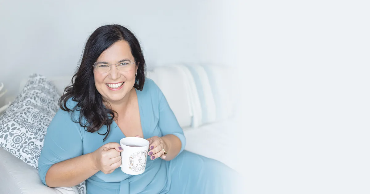 Maria Husch sitzt auf Bett in hellblauer Bluse mit Kaffeetasse