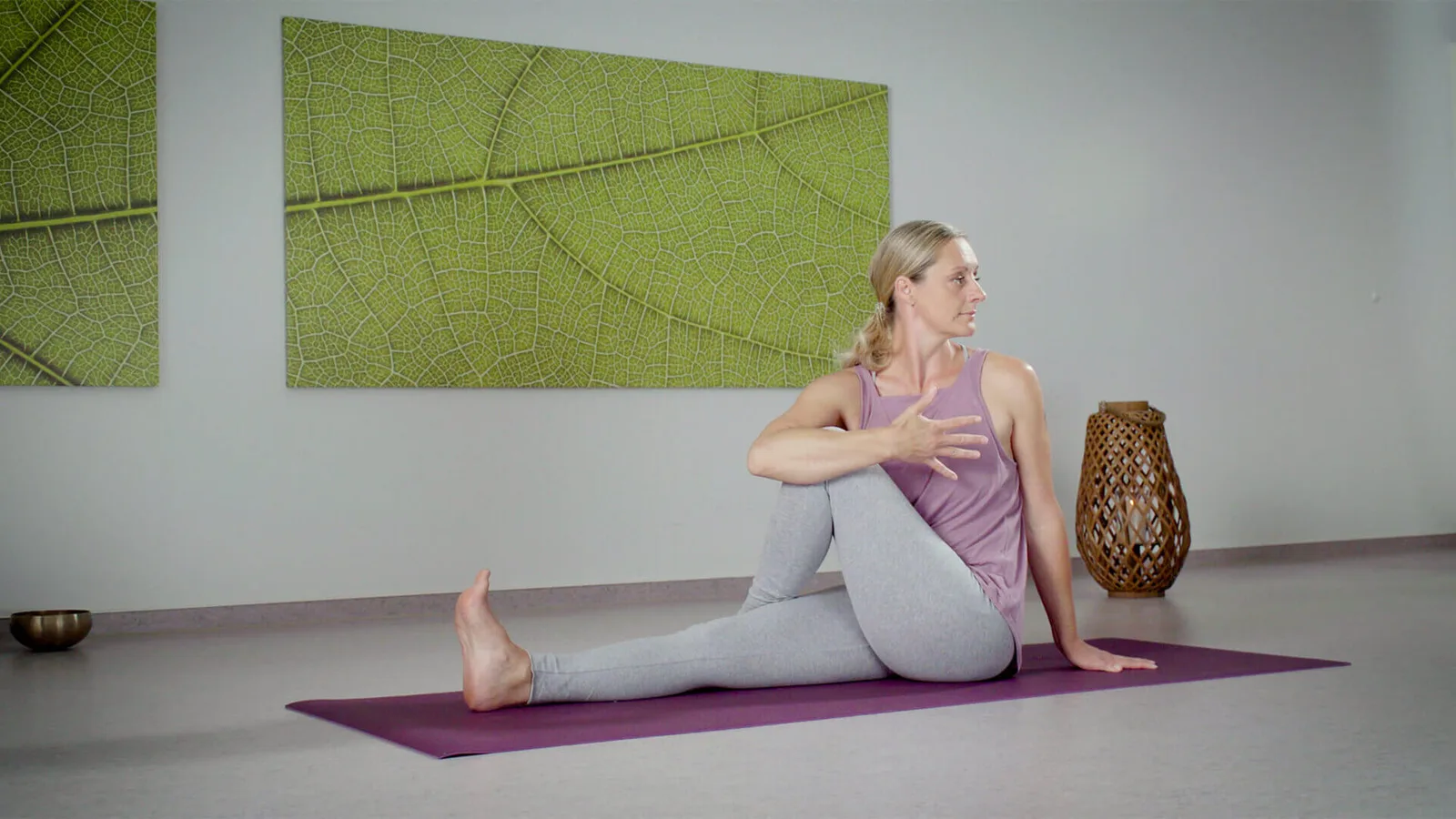 Frau in Yogaposition auf violetter Matte vor grünem Blatt-Kunstwerk