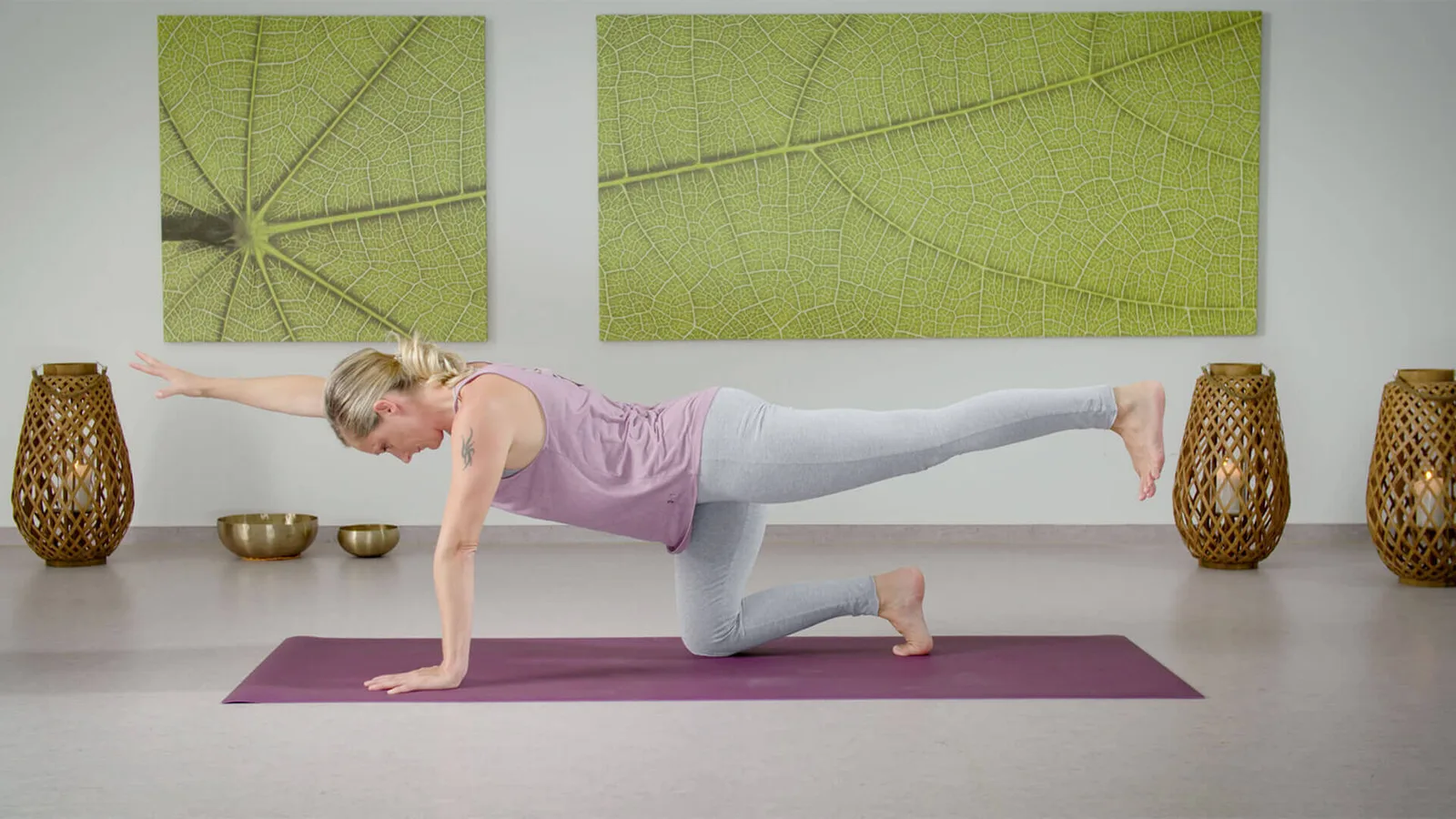 Frau in Yoga-Plankenposition auf violetter Matte mit grünen Blatt-Wandbildern