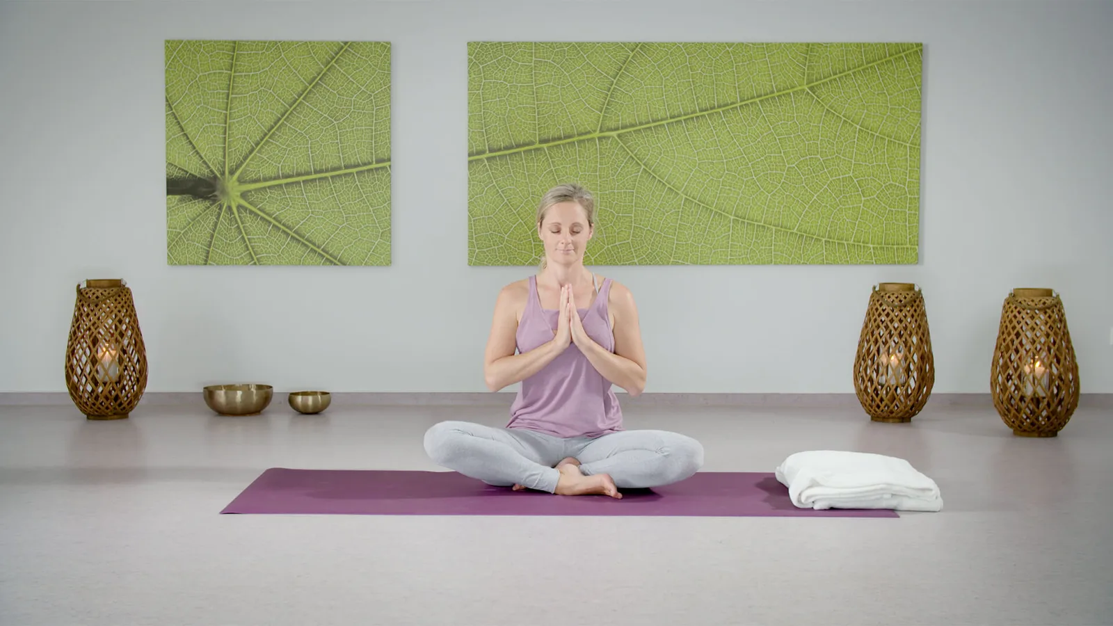 Frau in Meditationshaltung auf Yogamatte mit Namaste-Geste