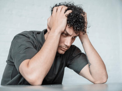 Mann mit gesenktem Blick, hält Kopf mit Händen – Burnout-Symptome