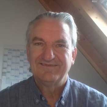 Porträtfoto von Urs Wirths, älterer männlicher Speaker mit grauem Haar in blauem Hemd