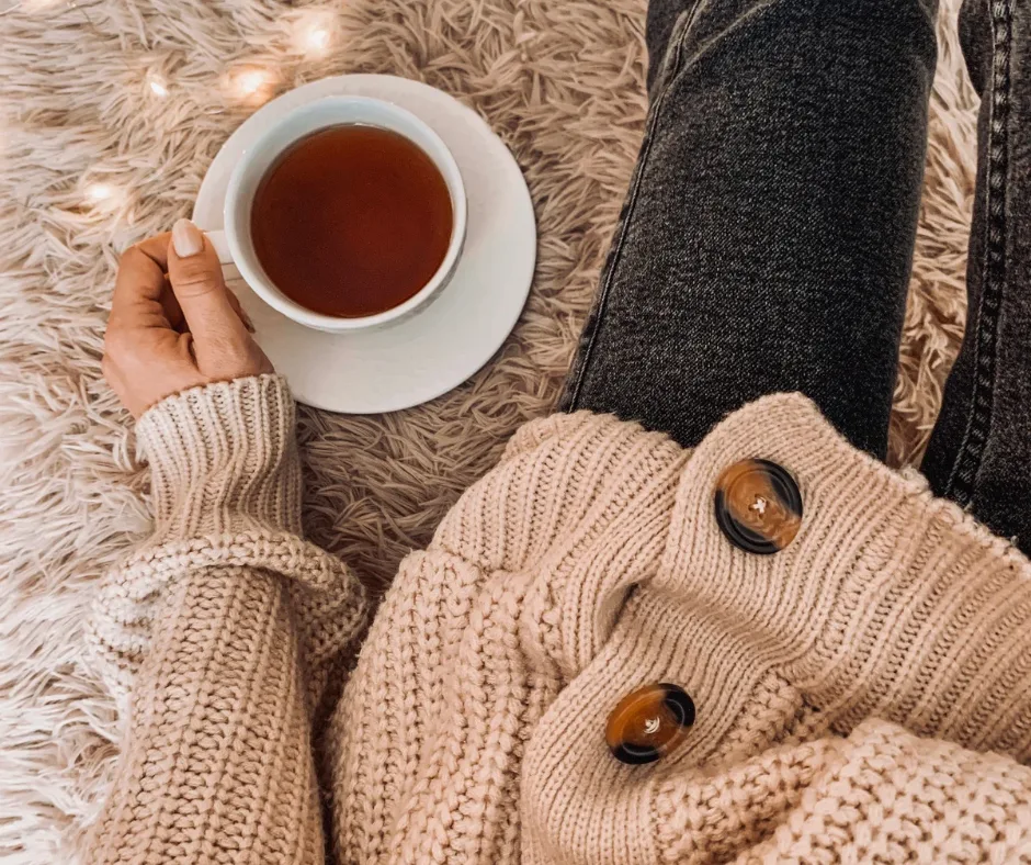 Healing Day – Selbstheilungstag mit Anleitung von Katja Demming 3 Frauenhände halten Tasse mit Tee auf Flokati-Teppich, gemütliche Herbst-Winteratmosphäre