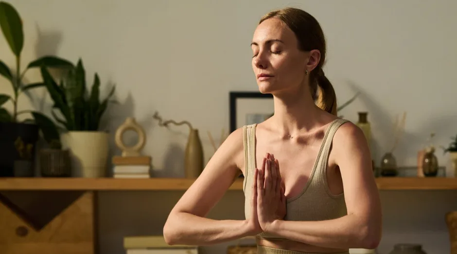 Healing Day – Selbstheilungstag mit Anleitung von Katja Demming 1 Frau in meditierender Pose mit Händen vor der Brust in minimalistischem Wohnzimmer mit Pflanzen