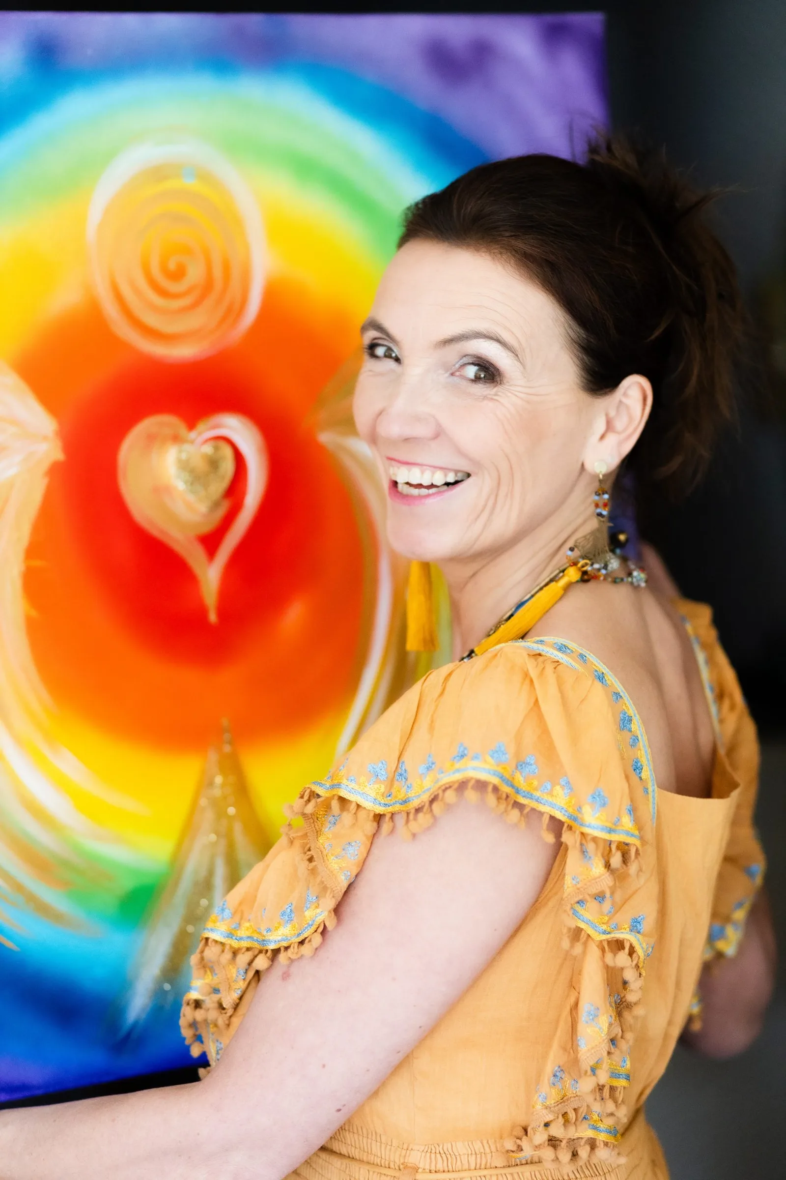 Carmen Duffner in gelbem Pailletten-Kleid vor Regenbogen-Chakra-Energiebild, Räucherstab