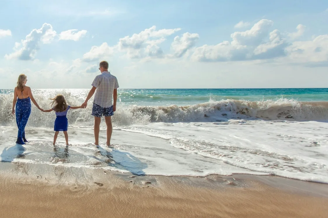 Familie mit zwei Kindern watet hand in hand ins Meer bei Tageslicht