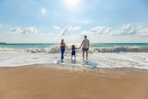 Familie mit zwei Kindern watet hand in hand ins Meer bei Tageslicht