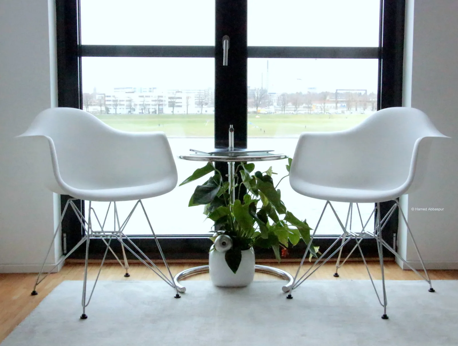 Modernes Therapie-Ambiente mit zwei weißen Designerstühlen, Glastisch und grüner Pflanze vor großem Fenster mit Stadtblick