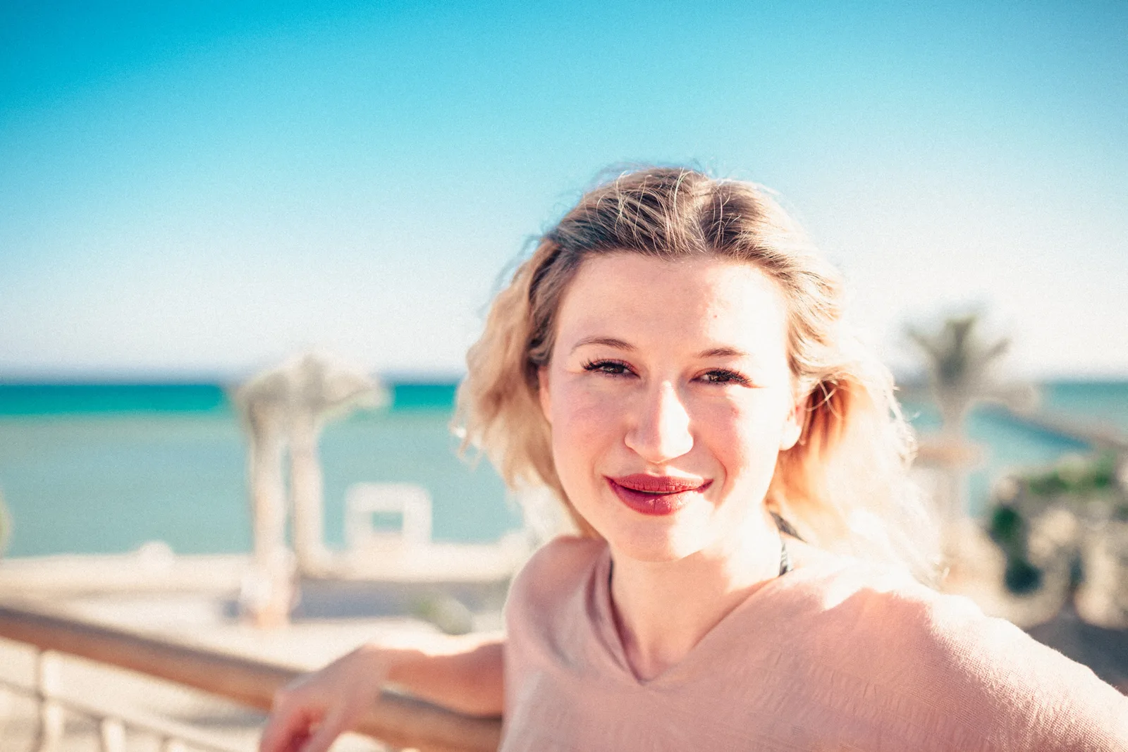 Frau mit blondem Haar lächelt am Meer mit Palmenbäumen, Porträt Nahaufnahme