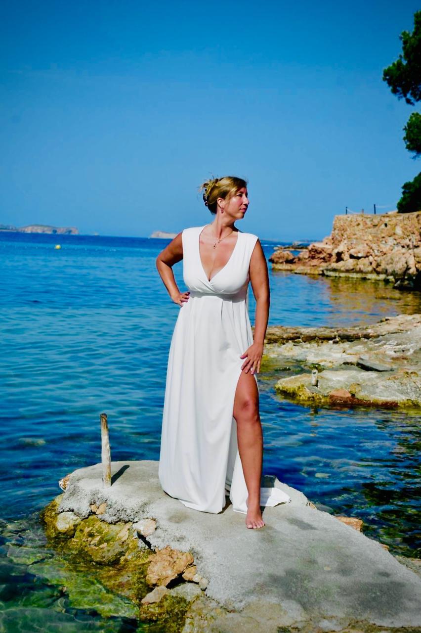 Stefanie Kosmalla in weißem Kleid am Strand vor blauem Meer und Felsen
