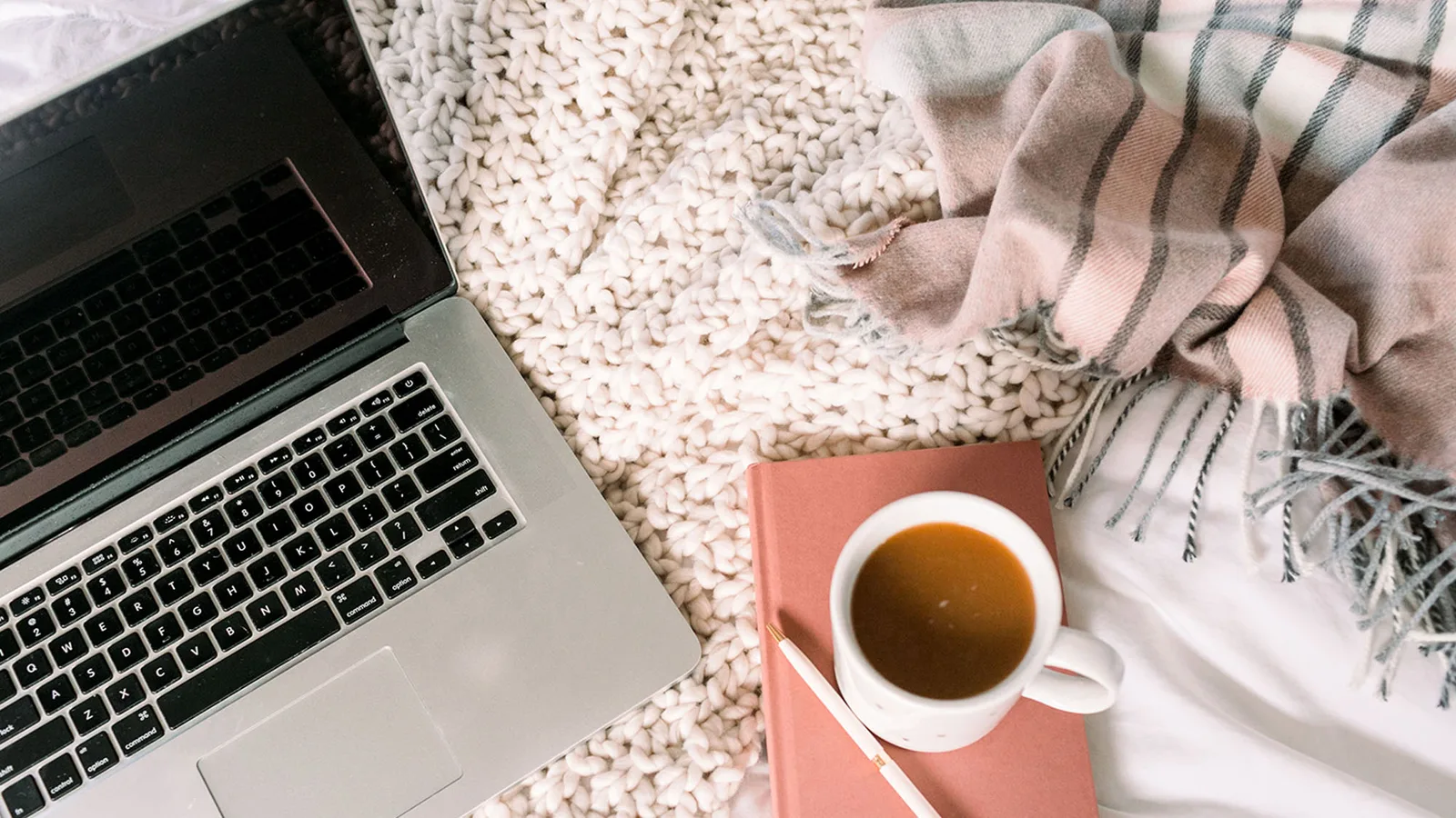 Laptop, Tasse Kaffee und Plaid-Decke auf cremefarbener Teppich-Oberfläche
