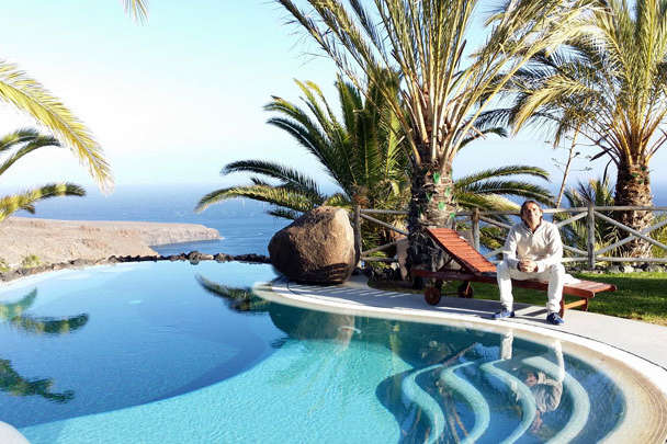 Mann in weißer Kleidung sitzt am Pool mit Meerblick und Palmen