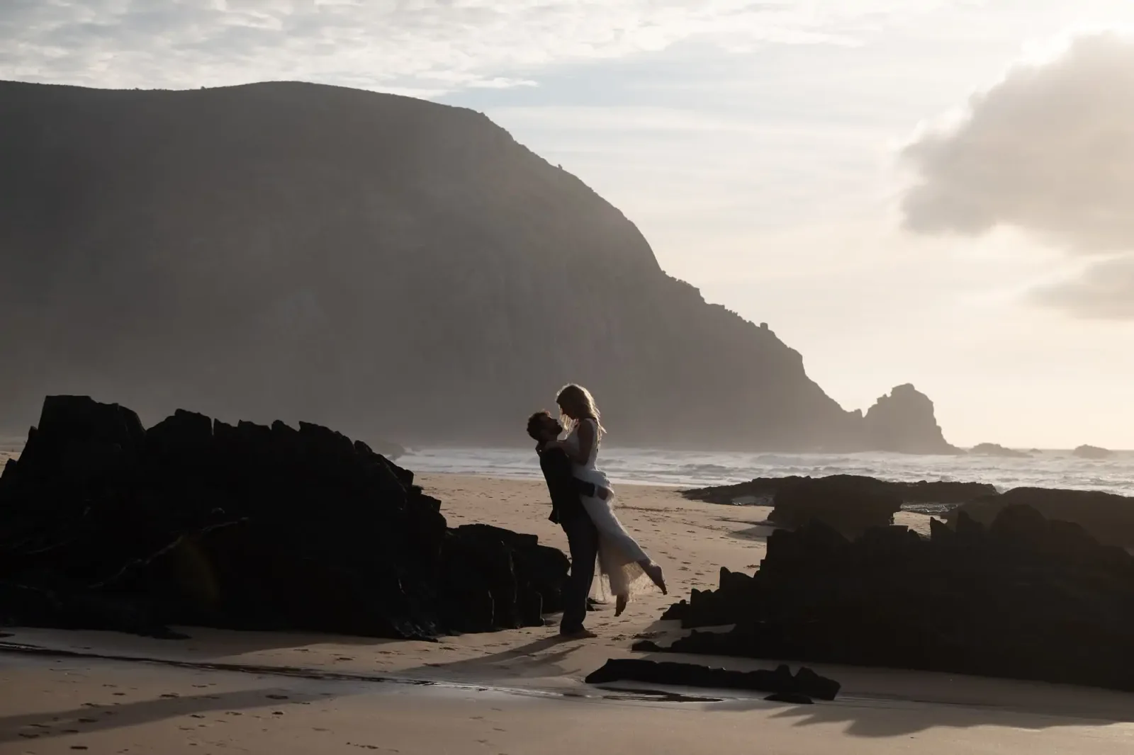 Brautpaar auf felsigem Strand mit Meereslandschaft und Klippen im Hintergrund, Silhouette