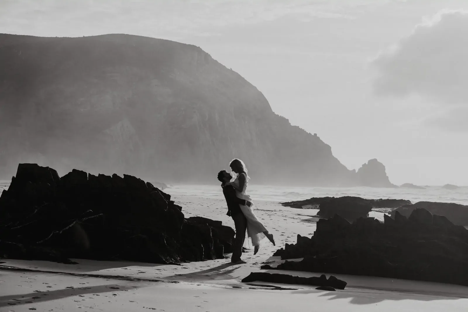 Braut und Bräutigam auf felsigem Strand, Schwarzweiß-Fotografie, dramatische Klippen