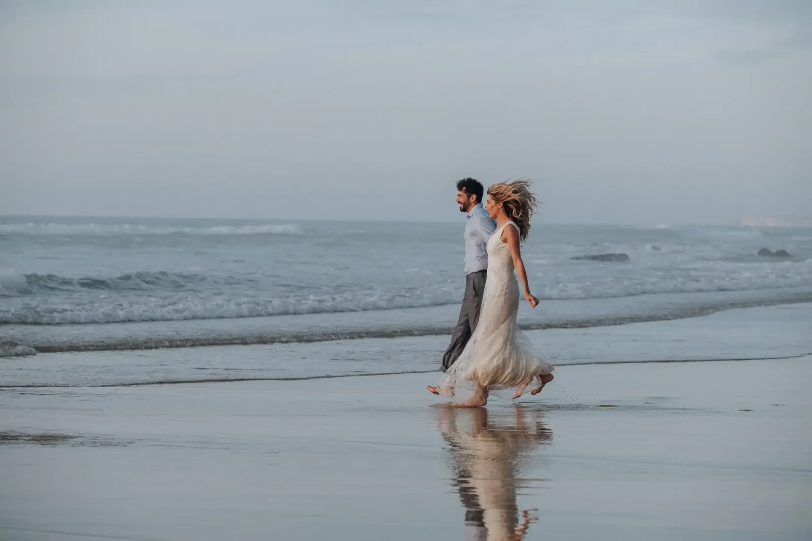 Brautpaar läuft am Strand, warme Beleuchtung, Meer und Himmel, Portrait