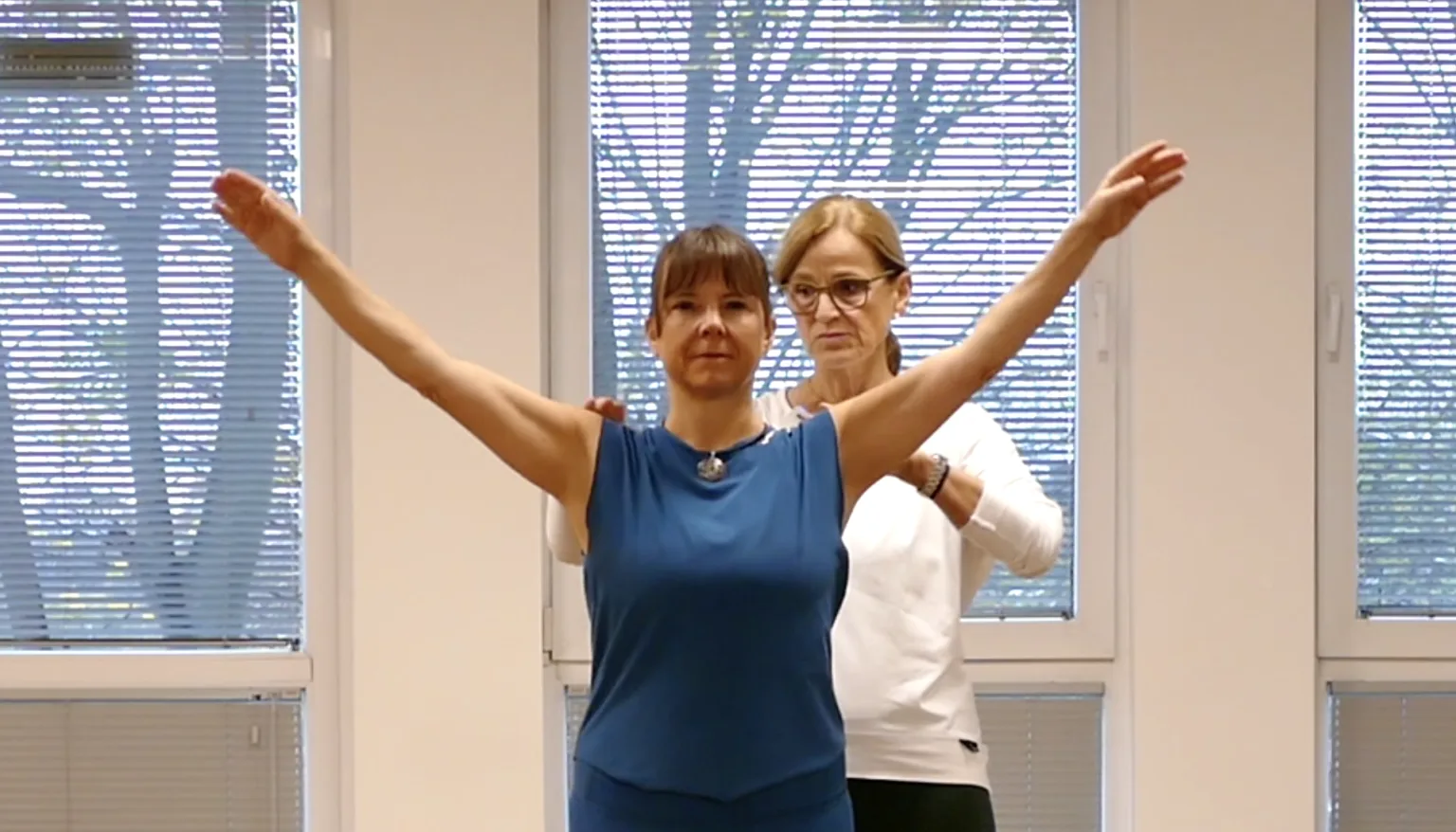 Zwei Frauen führen Pilates-Schulterübung durch, eine hebt beide Arme zur Seite