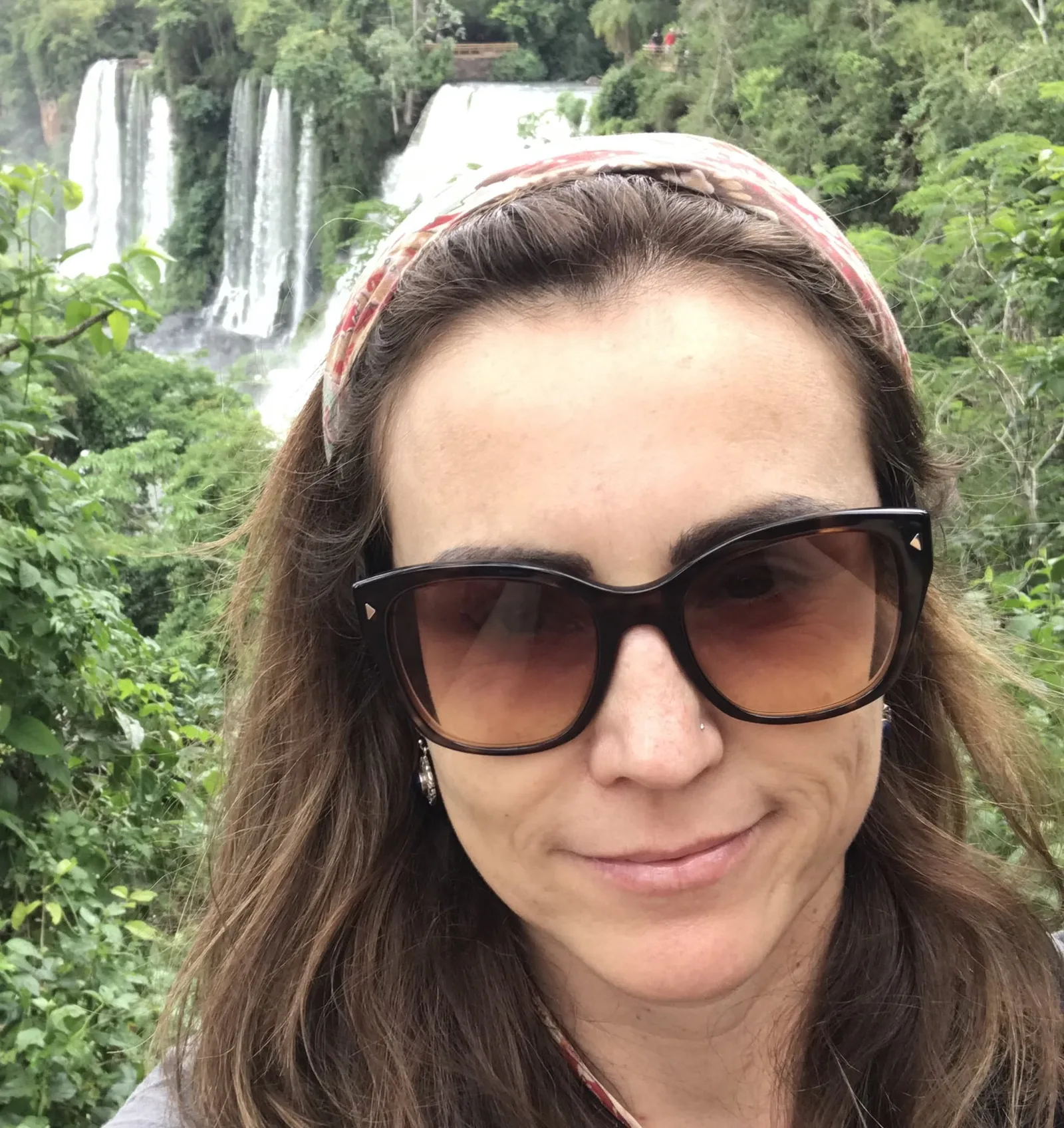 Frau mit braunen Haaren, Sonnenbrille und Stirnband, Wasserfall im Hintergrund
