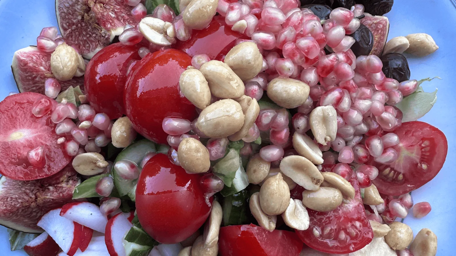 Farbenfrohe Anordnung von roten Tomaten, rosa Grapefruit, Nüssen und Beeren auf blauem Hintergrund
