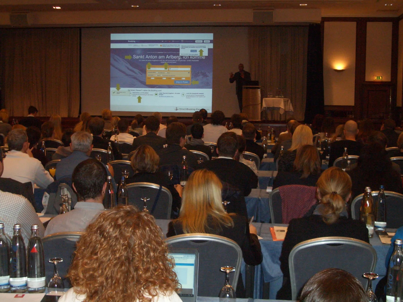 Konferenzpräsentation: Vortragssaal mit Zuhörern, Referent präsentiert Hotel-Website auf großer Leinwand, Konferenz zum Thema