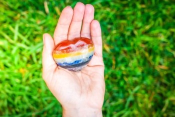 Hand mit regenbogenfarbenem Kristall auf grünem Gras