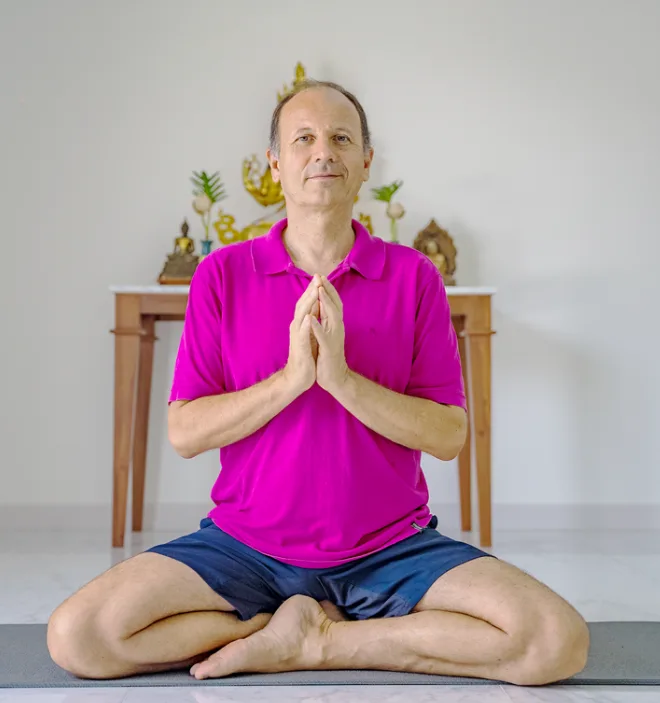 Mann im Meditationspose, rosa Hemd, vor Thai-Altar sitzend