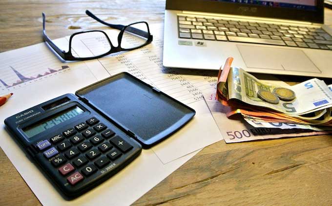 Schreibtisch mit Taschenrechner, Geldscheine, Brille, Laptop und Finanz-Unterlagen