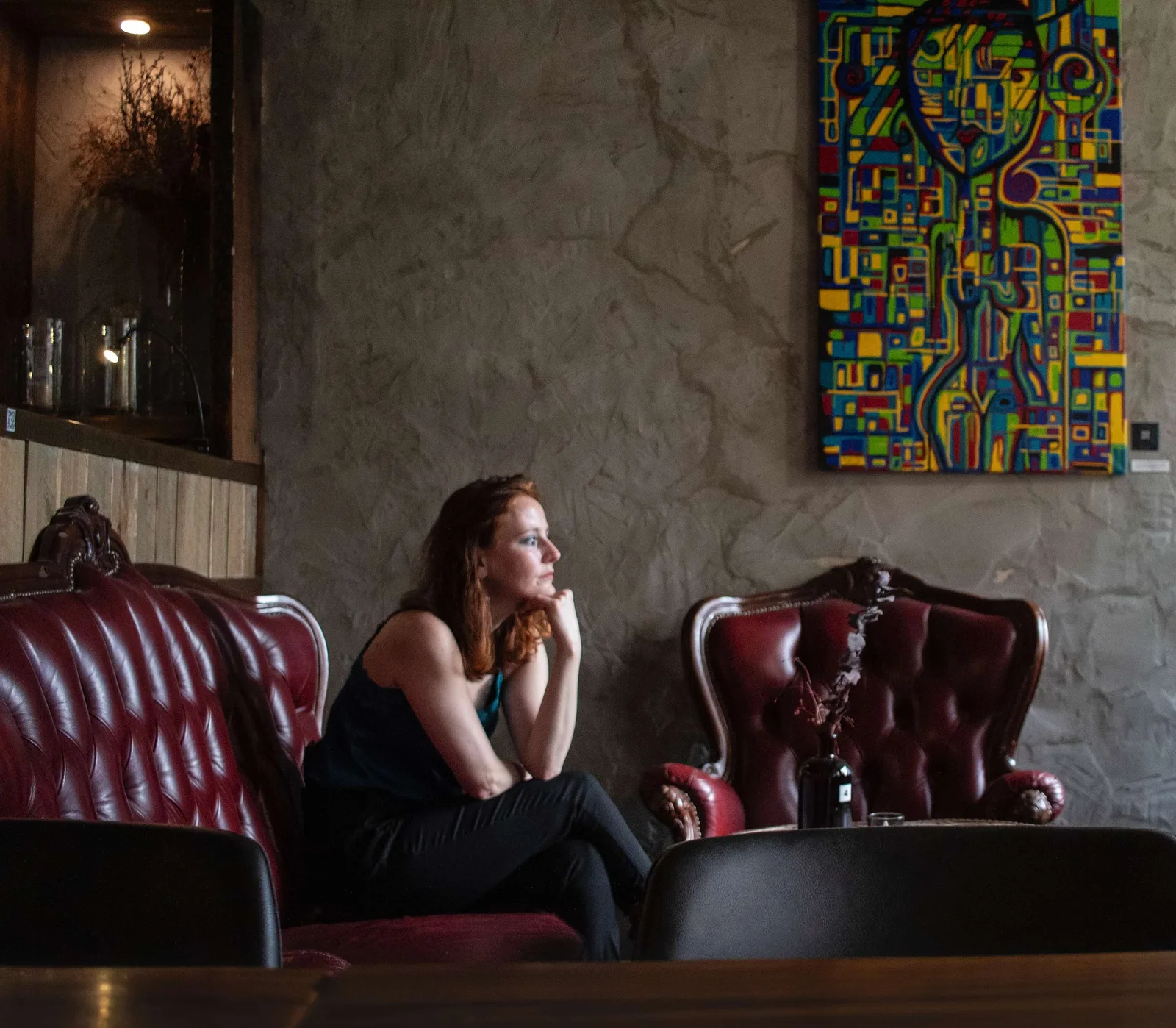 Lounge-Bereich mit roten Ledersofas unter buntem abstraktem Gemälde in Blau, Rot, Gelb und Grün