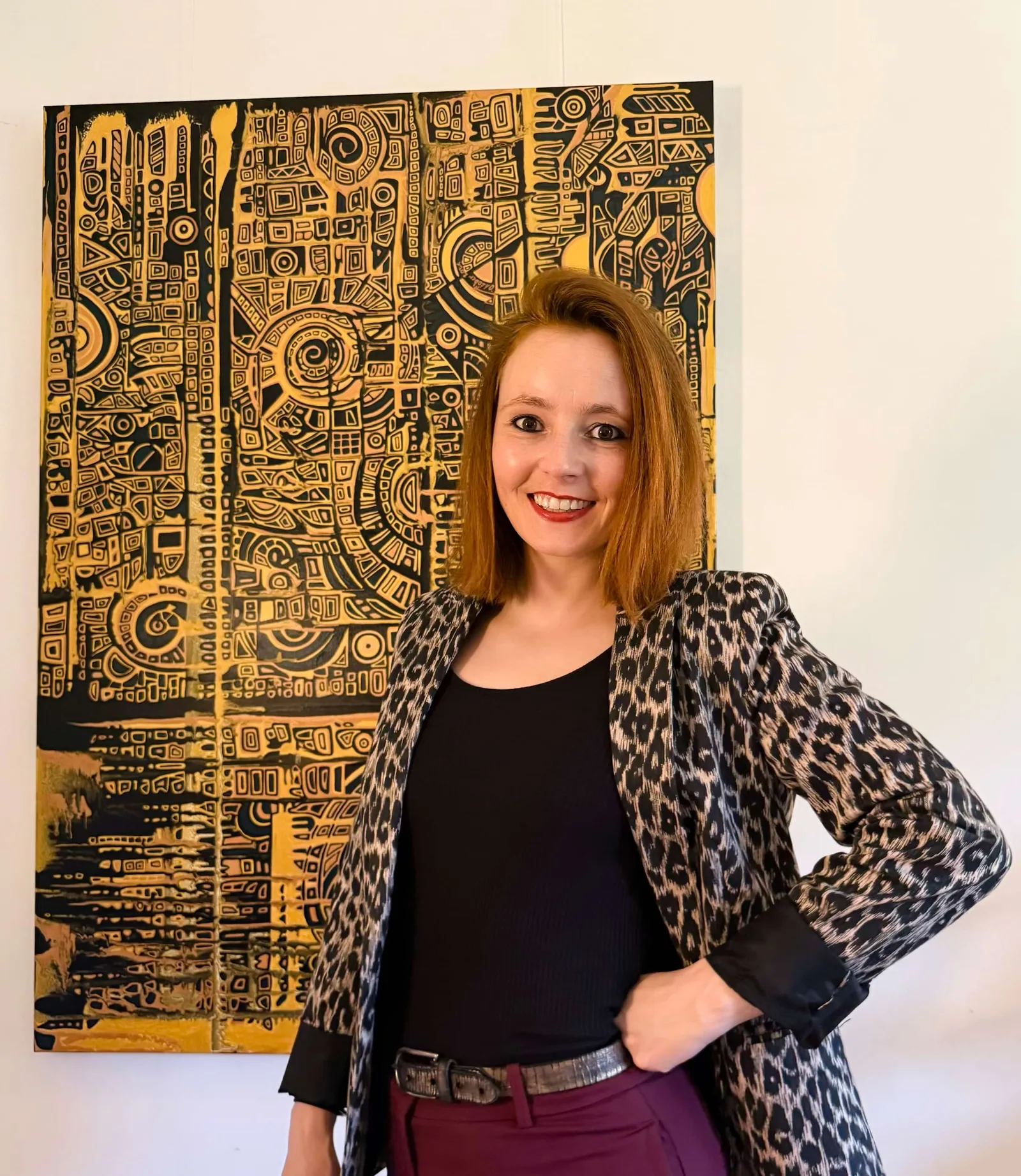 Frau mit rötlich-braunem Haar vor gold-schwarzem Kunstwerk, Leoparden-Blazer
