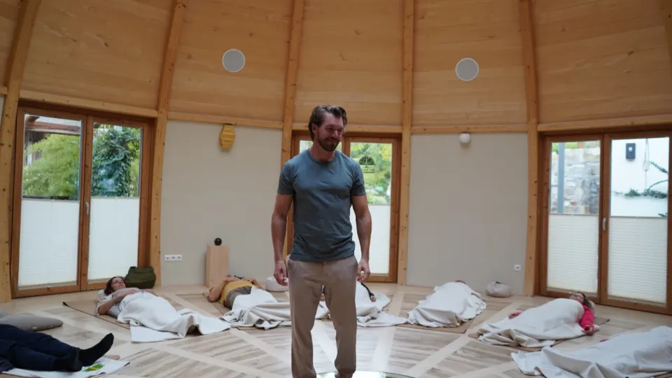 Fabian Ries unterrichtet eine Hypnobreath-Gruppe in Yoga-Positionen auf gepolsterten Matten in holzverkleideter Halle