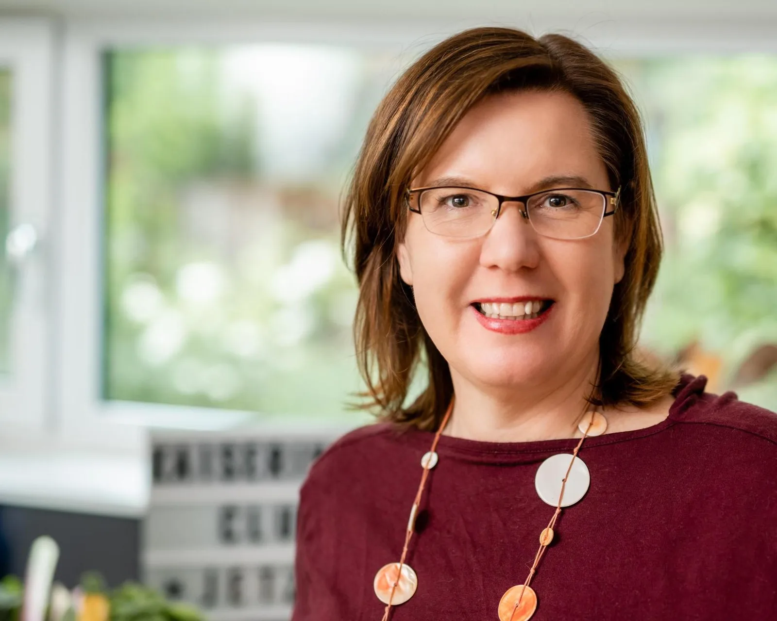 Porträt von Dr. Claudia Nichterl mit braunem Haar, Brille, Lächeln, burgundy Pullover vor grünem unscharfem Hintergrund