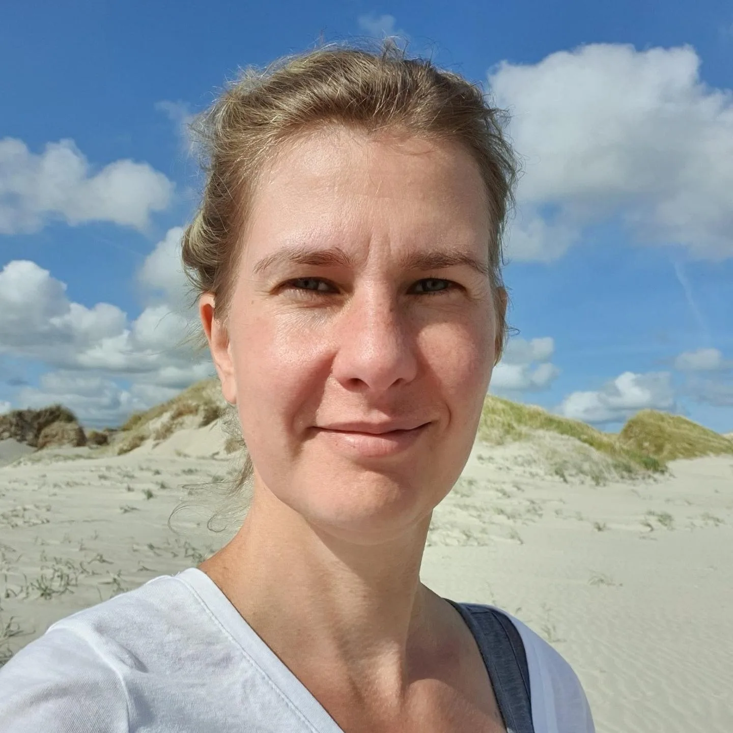 Frau blondes Haar Strandporträt mit blauem Himmel und Dünen im Hintergrund, lächelnd
