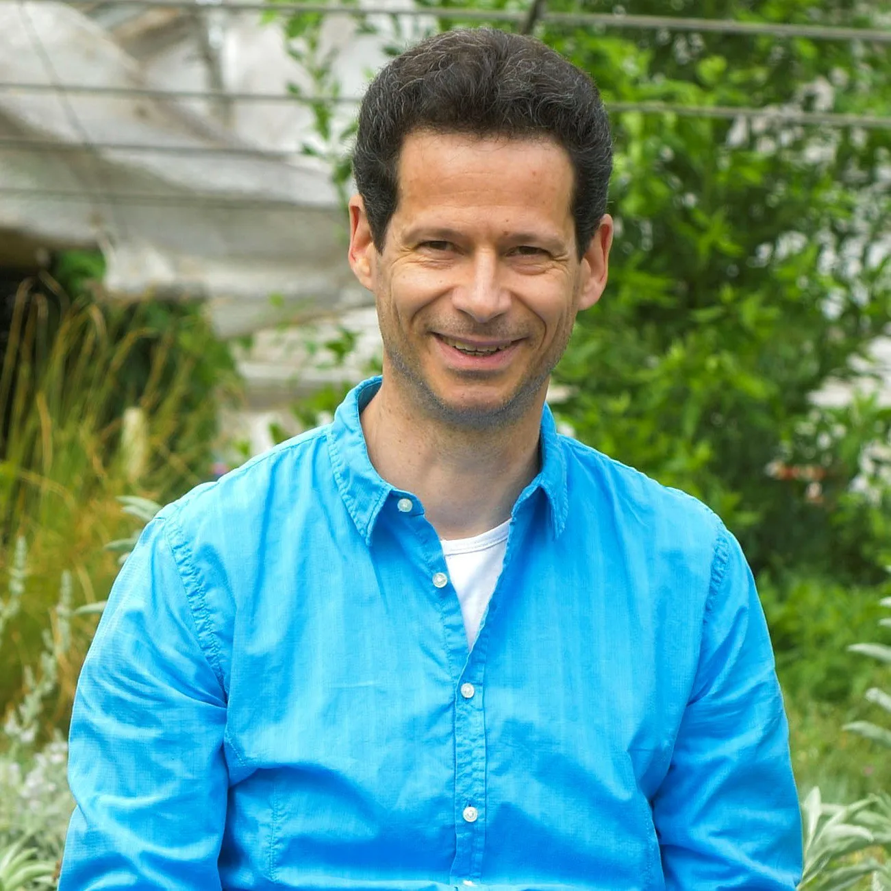 Intensivwochenende 2.0 mit Dr. Hartmut Fischer 4 Dr. Hartmut Fischer Portrait, Mann mit dunklem Haar in hellblauem Hemd vor grünem Pflanzenhintergrund